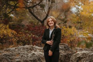 Portrait against autumn foliage wearing black velvet jacket on rocky outcrop.
