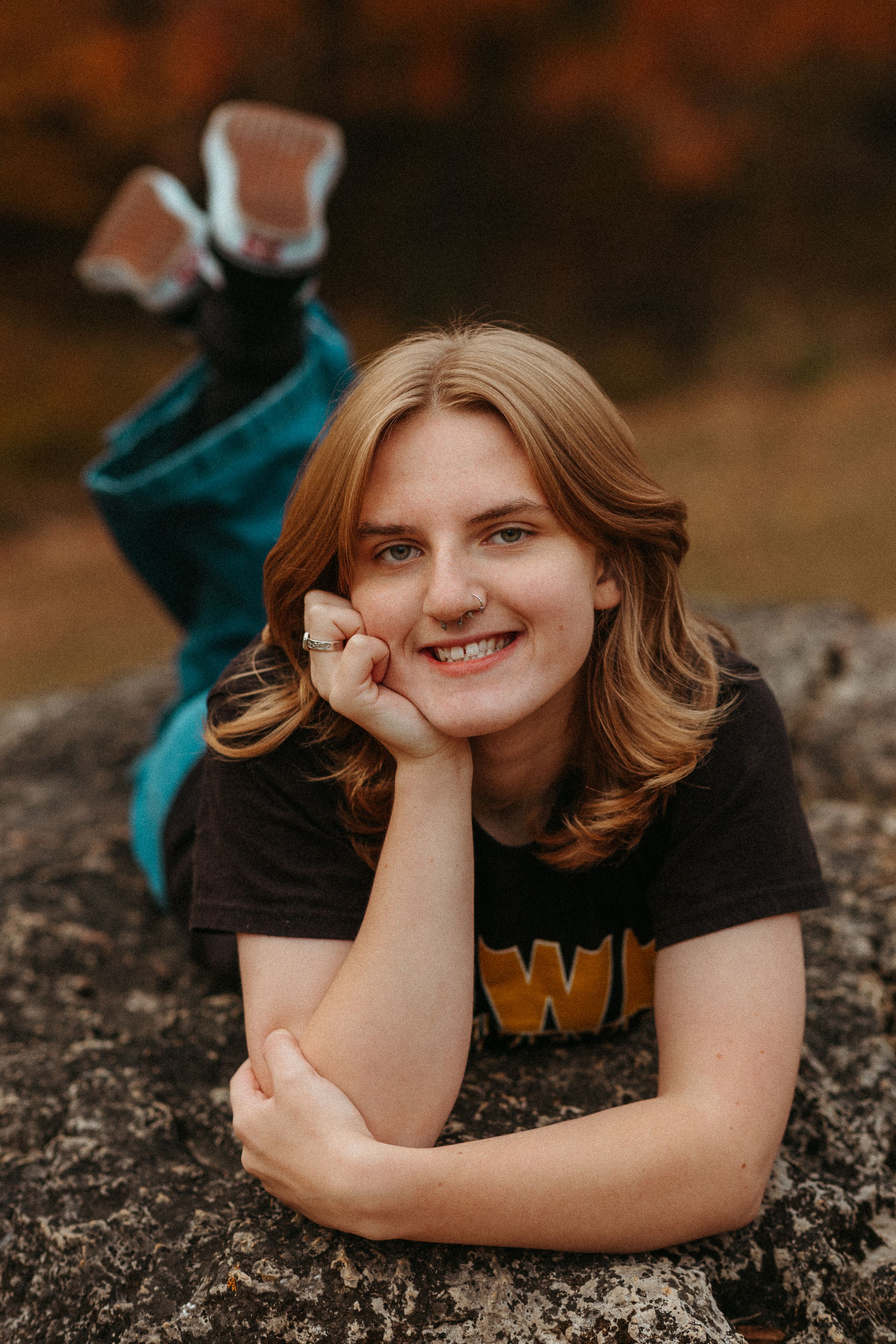 Person relaxing on rock outdoors wearing black t-shirt with autumn scenery in background.