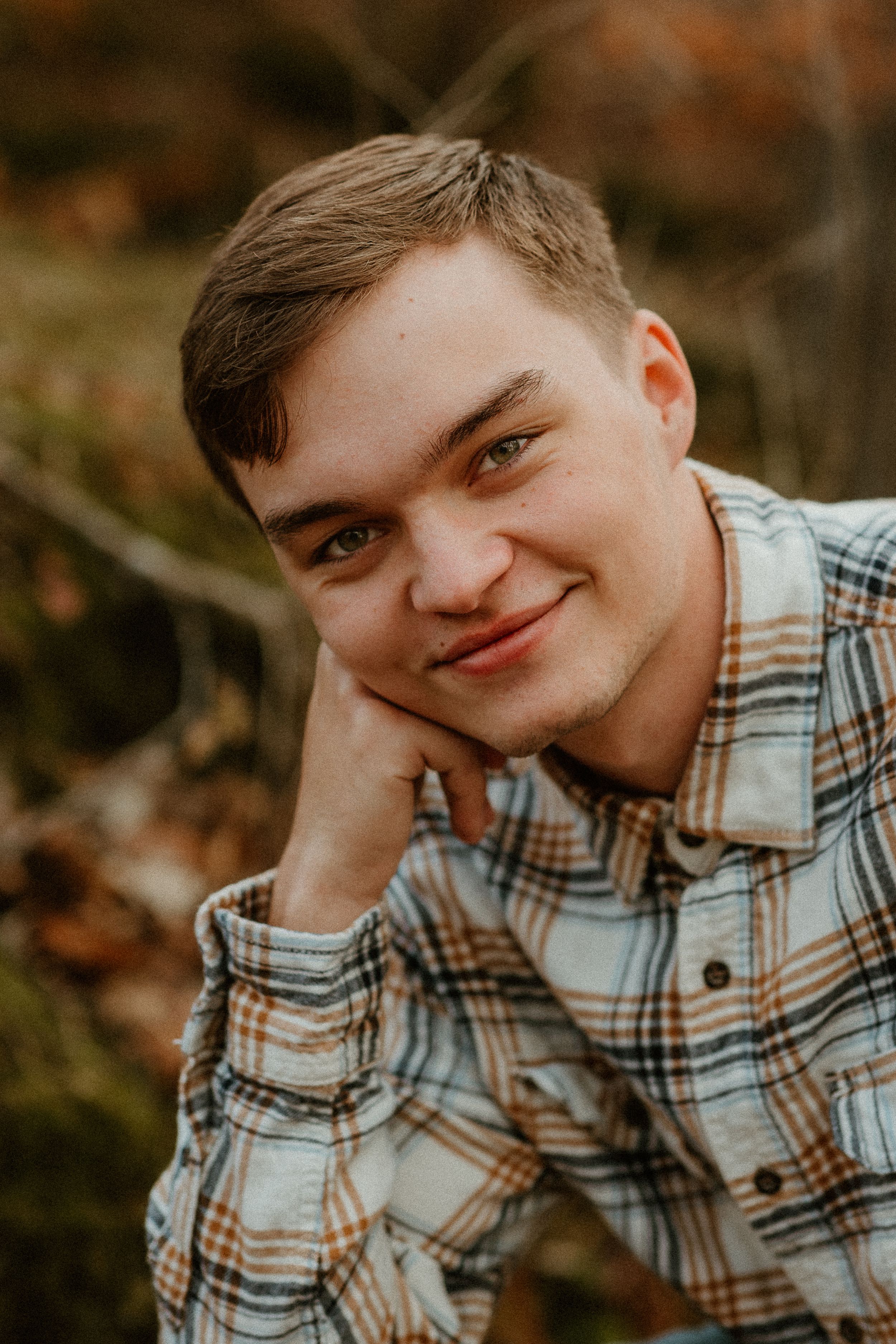 A casual portrait of someone in a plaid shirt with an autumn background.