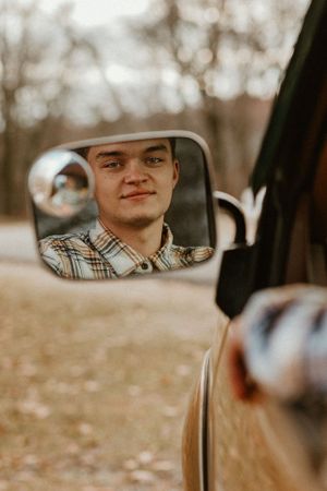 A reflection in a car side mirror showing someone in a plaid shirt.