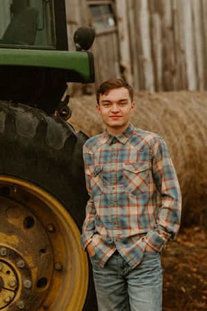 Someone posing beside a large green tractor on a farm.