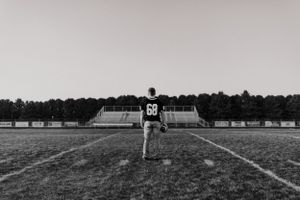 Figure standing alone on empty football field in black and white photograph.