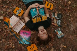 Overhead shot of books and reading materials arranged on fallen autumn leaves.
