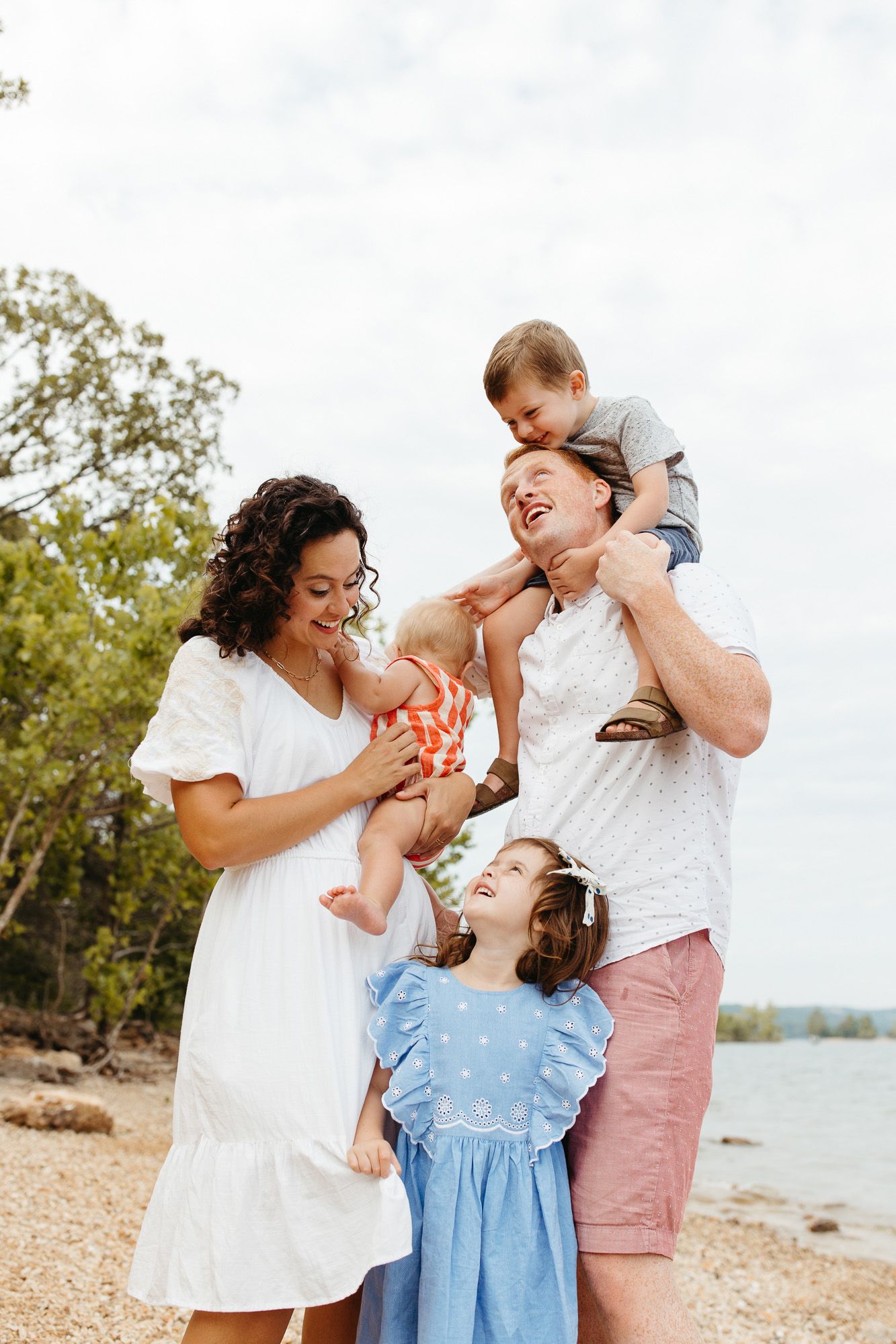 A joyful family shares a playful moment together on a beach with trees in the background.