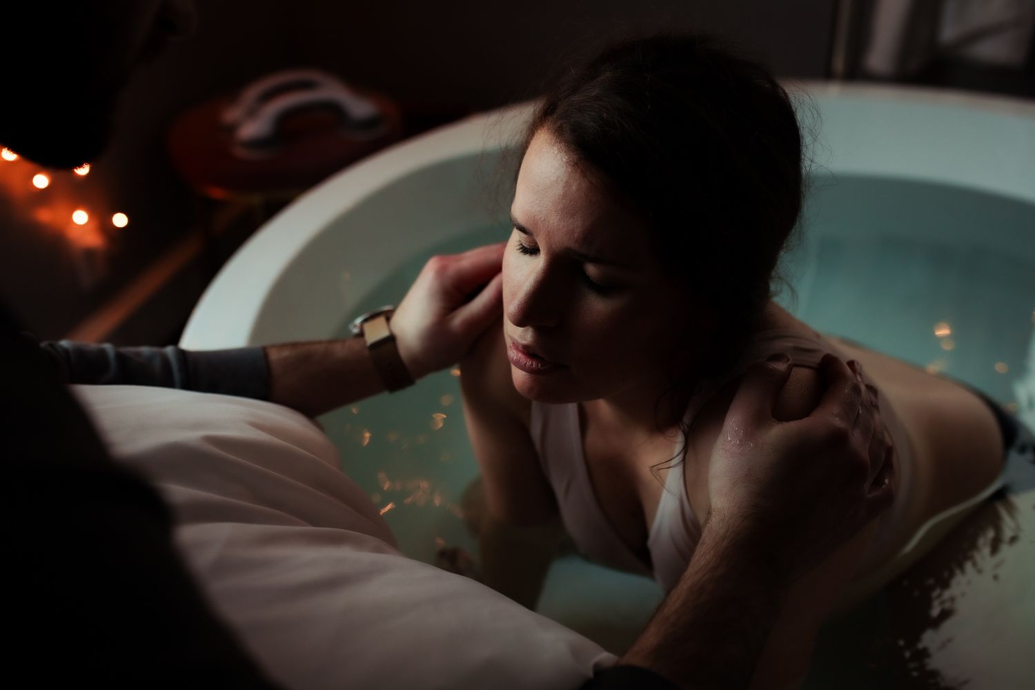 MOTHER-LABORS-IN-BIRTH-TUB-AT-ORIGINS-DALLAS-WITH-DADS-HANDS-ON-HER-SHOULDERS-MID-CONTRACTION