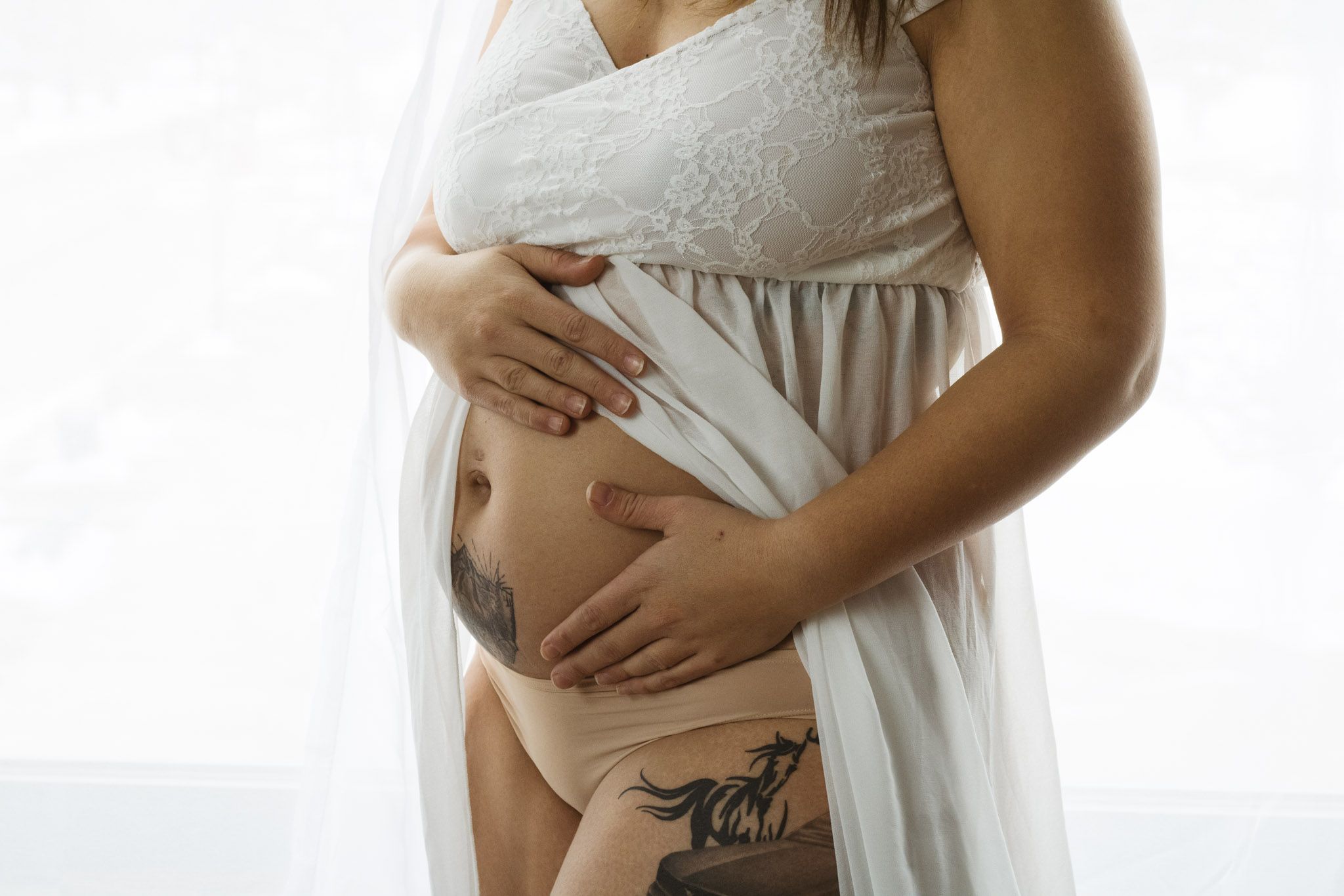 Close-up shot of hands cradling pregnant belly with visible tattoo.