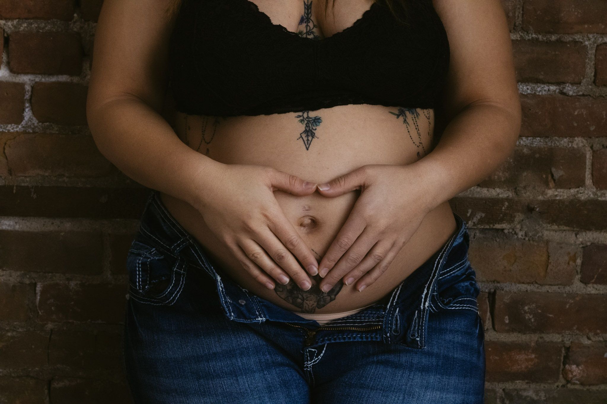 Close-up of hands forming heart shape over stomach with visible tattoo.