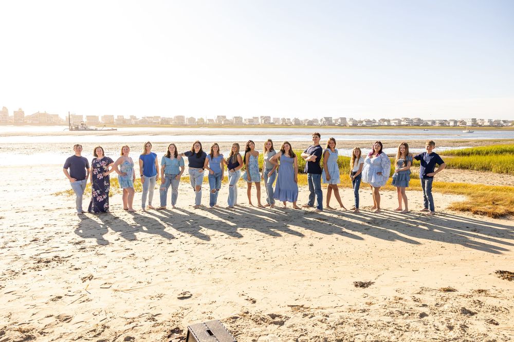 A group of people standing together on a sandy beach during sunset with wetlands in the background.