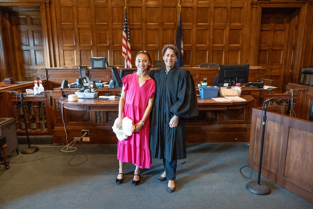People walking through a wood-paneled courtroom with ornate architectural details and traditional legal furnishings.