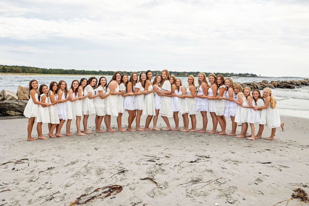 A group in white dresses poses together on a sandy beach during sunset creating a panoramic photo series.