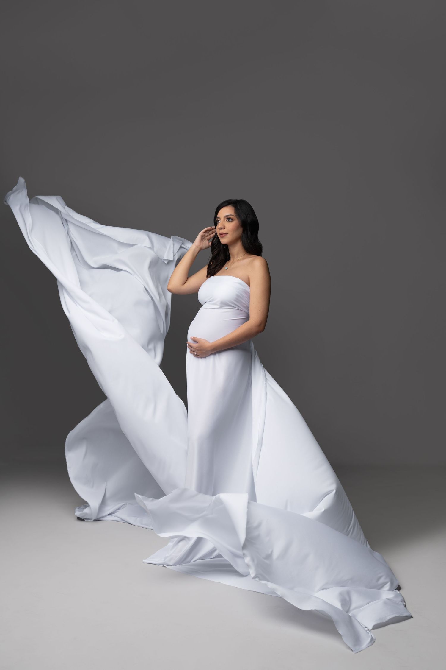 Maternity photo with flowing white fabric dramatically billowing around an expectant mother.