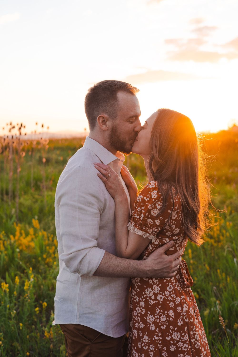 Romantic couple sharing a kiss in a wildflower field during golden hour sunset.