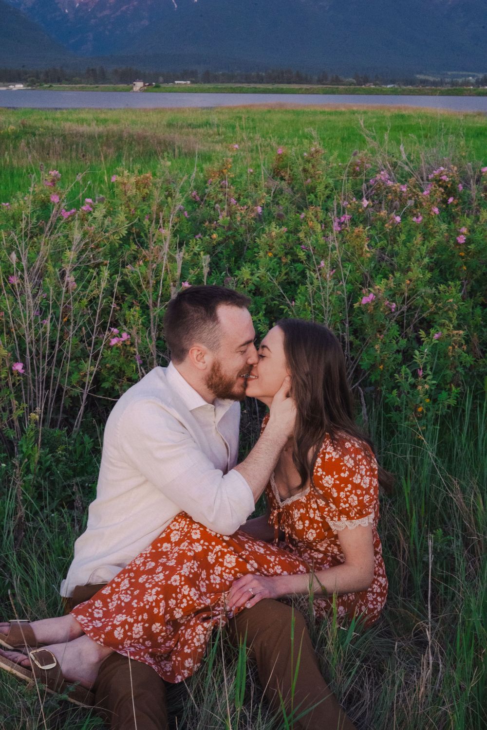 A romantic couple sharing tender moments in a field of tall grass and wildflowers at sunset.