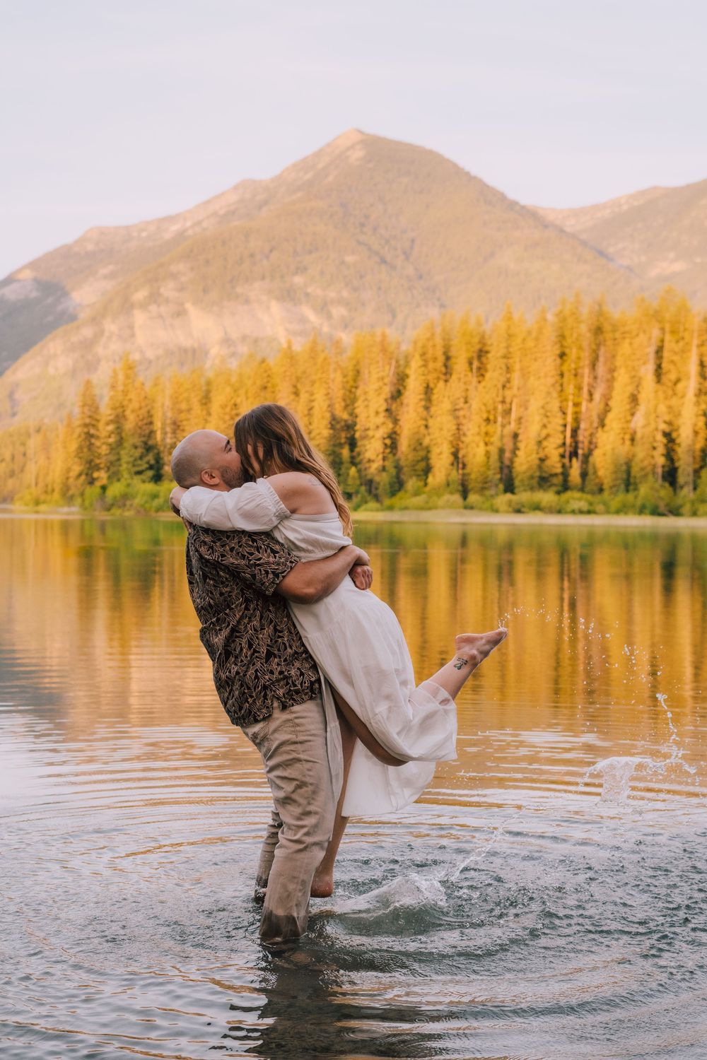 A romantic mountain lakeside embrace at sunset with golden larches reflecting in calm waters at Vermilion Lakes, Banff.
