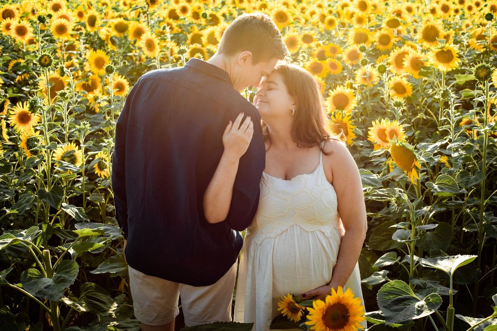In a sunflower field on Hayling Island, Hampshire, couple touch foreheads in the flowers at sunset during Maternity photo session.