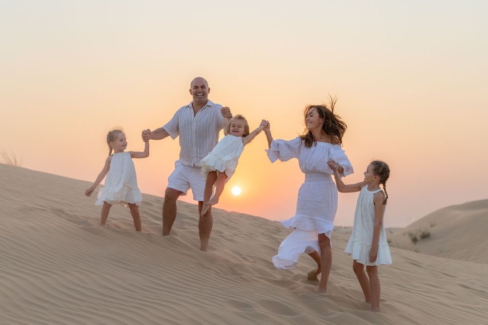 Beeautiful family portrait in the Dubai desert with the sunsetting in the background and the youngest child being swung in the air by parent