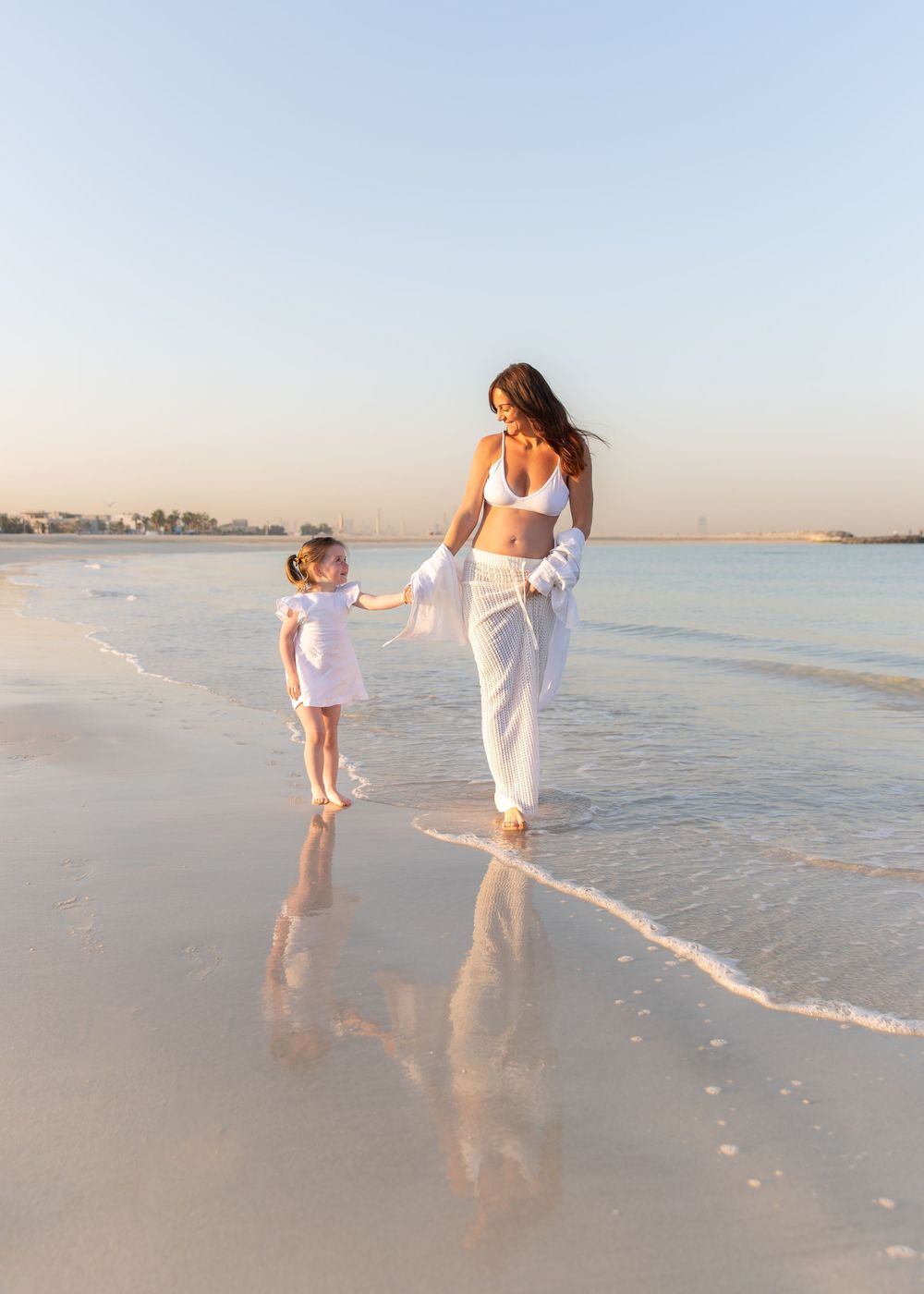 Mother and daughter walk hand in hand along the beach - candid, natural portrait taken during family, maternity shoot in dubai