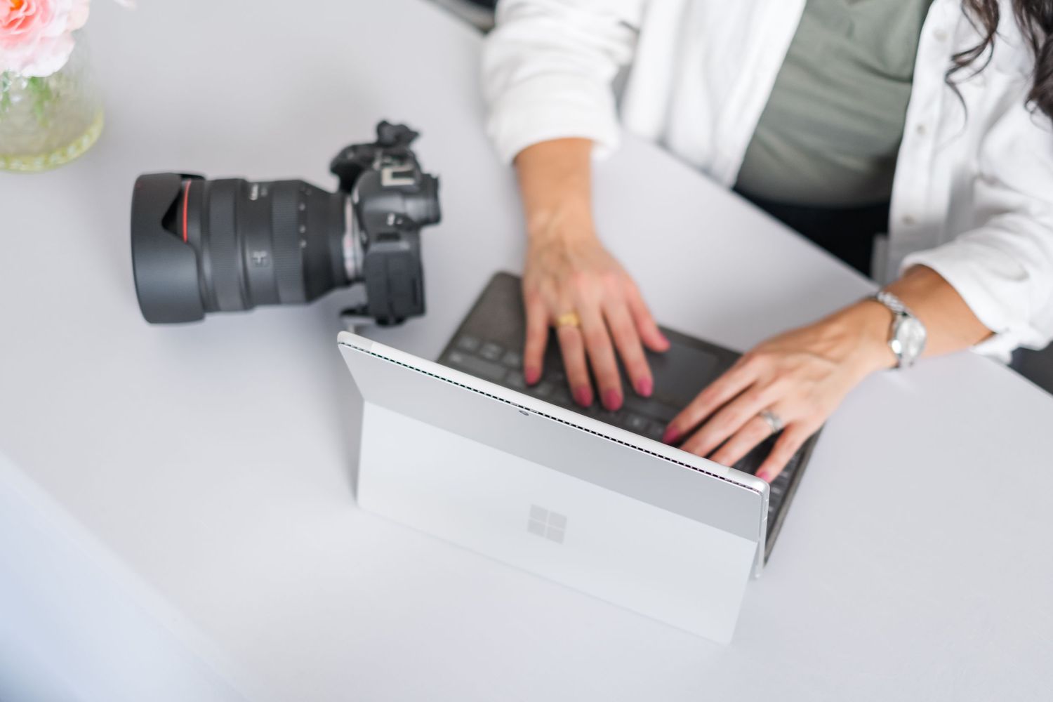 Photographer in red plaid shirt and white tank top takes photos with a digital camera in outdoor setting.