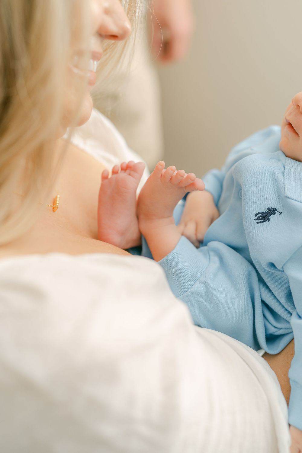 A small baby wearing a light blue outfit rests against someone in white clothing while being held.