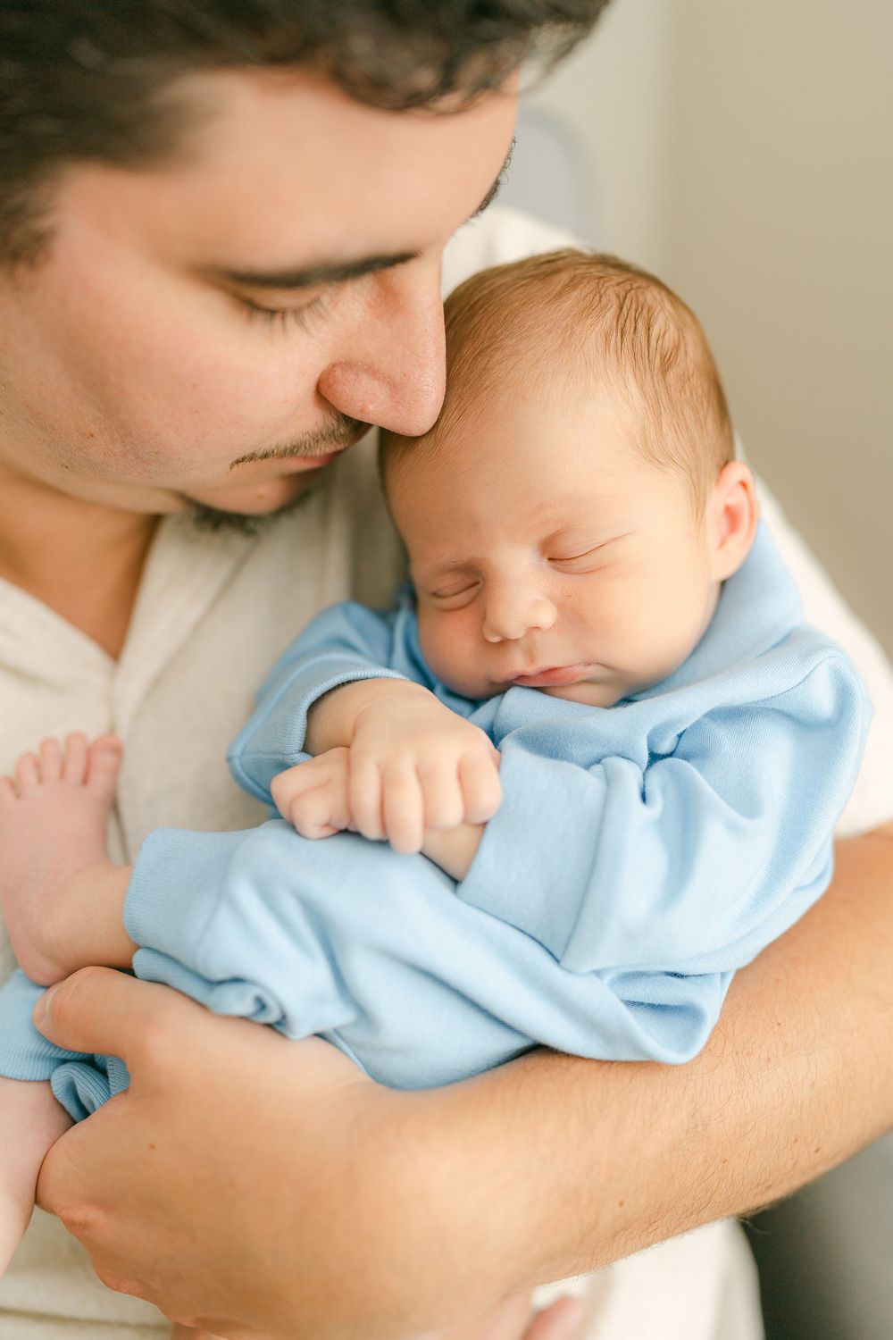 A tender sequence of photos showing a loving parent cradling and kissing a sleeping baby in light blue clothing.