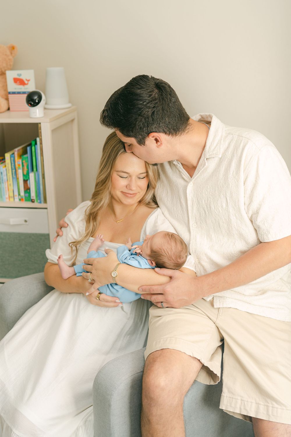 Parents in white clothing sharing tender moments with their newborn baby in a bright, cozy home setting.