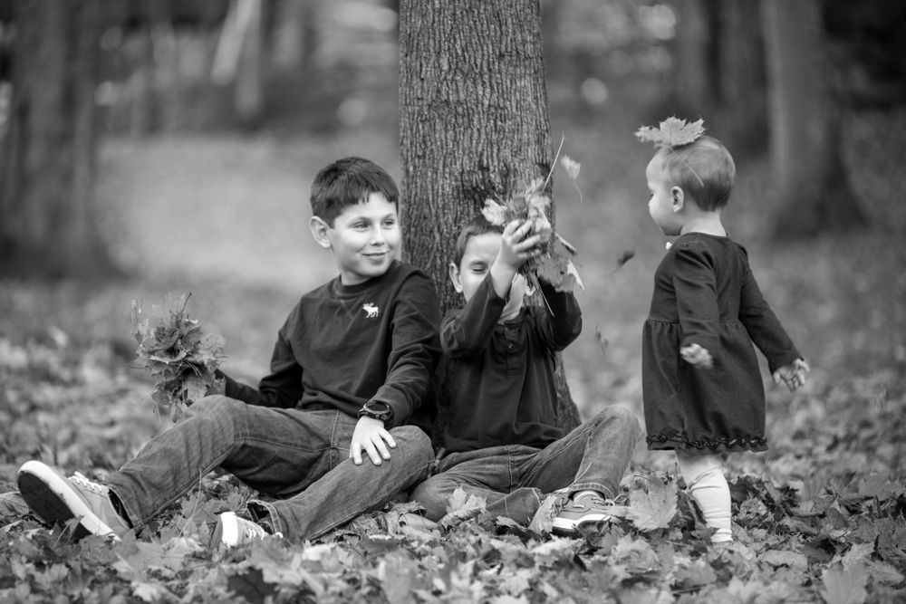 Black and white portrait of a playful family moment captured outdoors among fallen leaves.