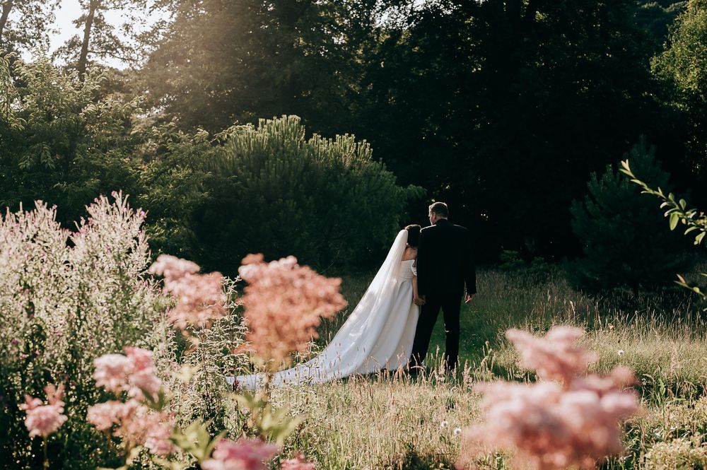Bride and groom walking hand in hand through a lush garden with wildflowers and soft golden sunlight.