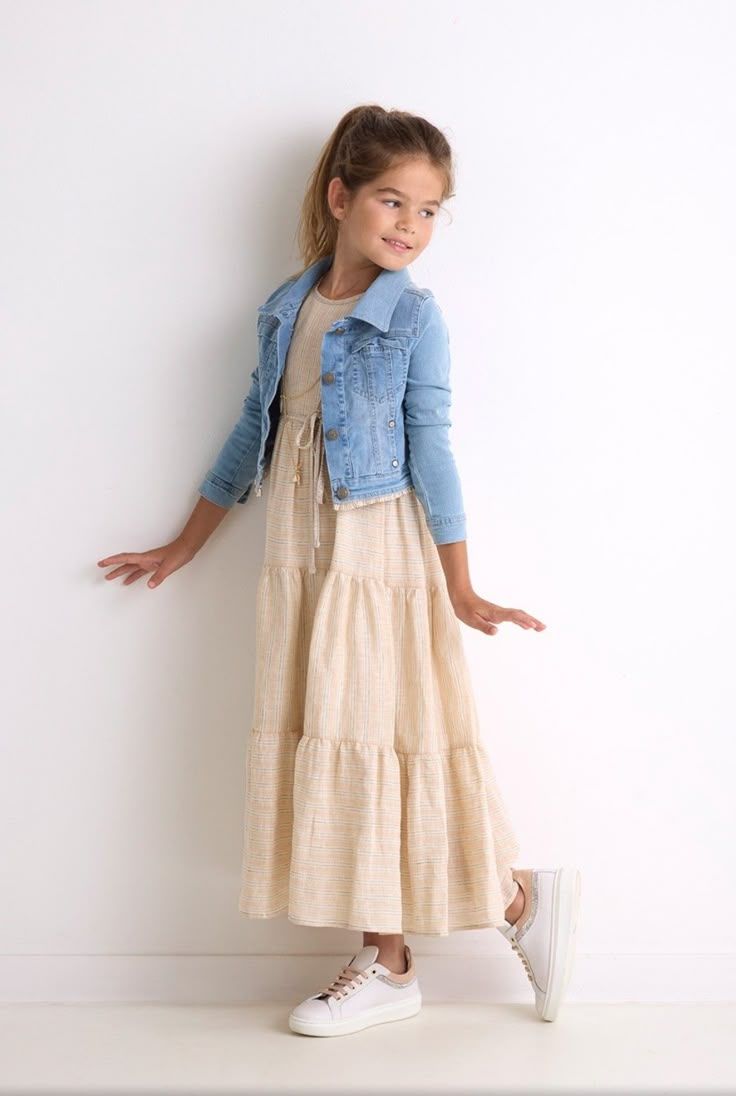 Young girl wearing a beige tiered maxi dress with a light blue denim jacket and white sneakers.