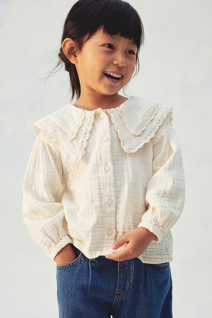 Young girl wearing a cream textured blouse with lace peter pan collar and blue jeans, smiling cheerfully.