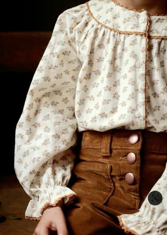 Child wearing a floral cream blouse with lace trim and brown corduroy button-front skirt.