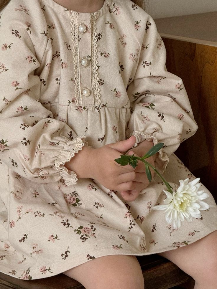 Young girl in a beige floral long-sleeve dress holding a white chrysanthemum flower.
