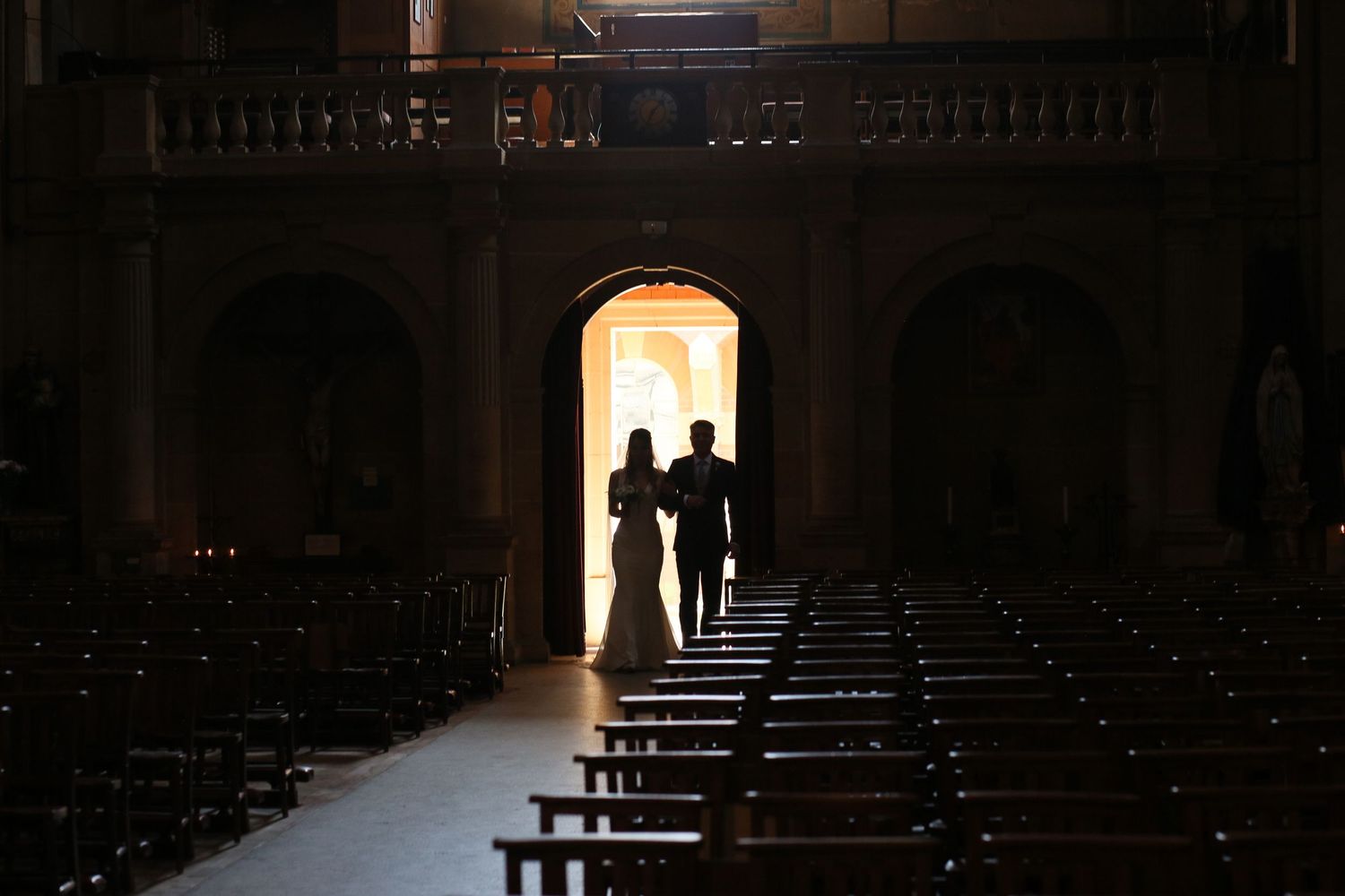 Silhouetted figures in a grand church with dramatic backlighting through an arched doorway.
