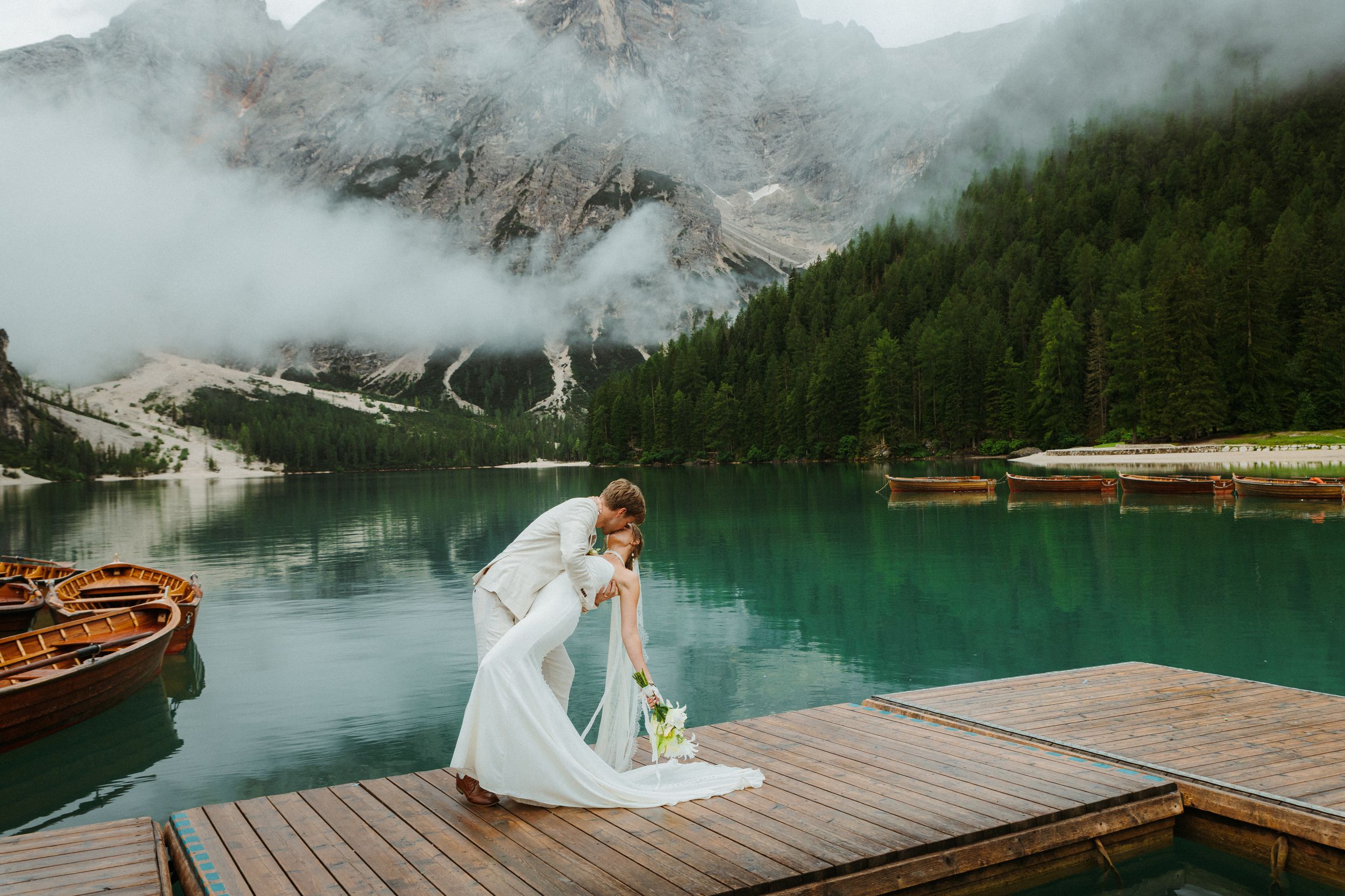 Bride and groom kiss on a wooden dock by a misty Queenstown lake - moody fine-art wedding moment by Selah Weddings.