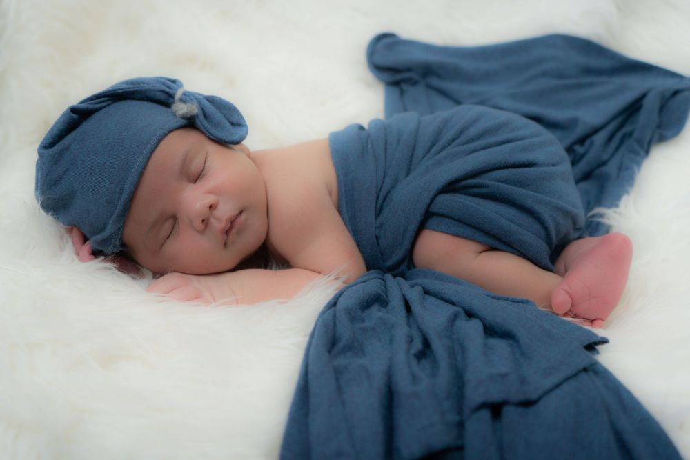 A sleeping baby in a navy blue outfit is peacefully resting on white bedding.
