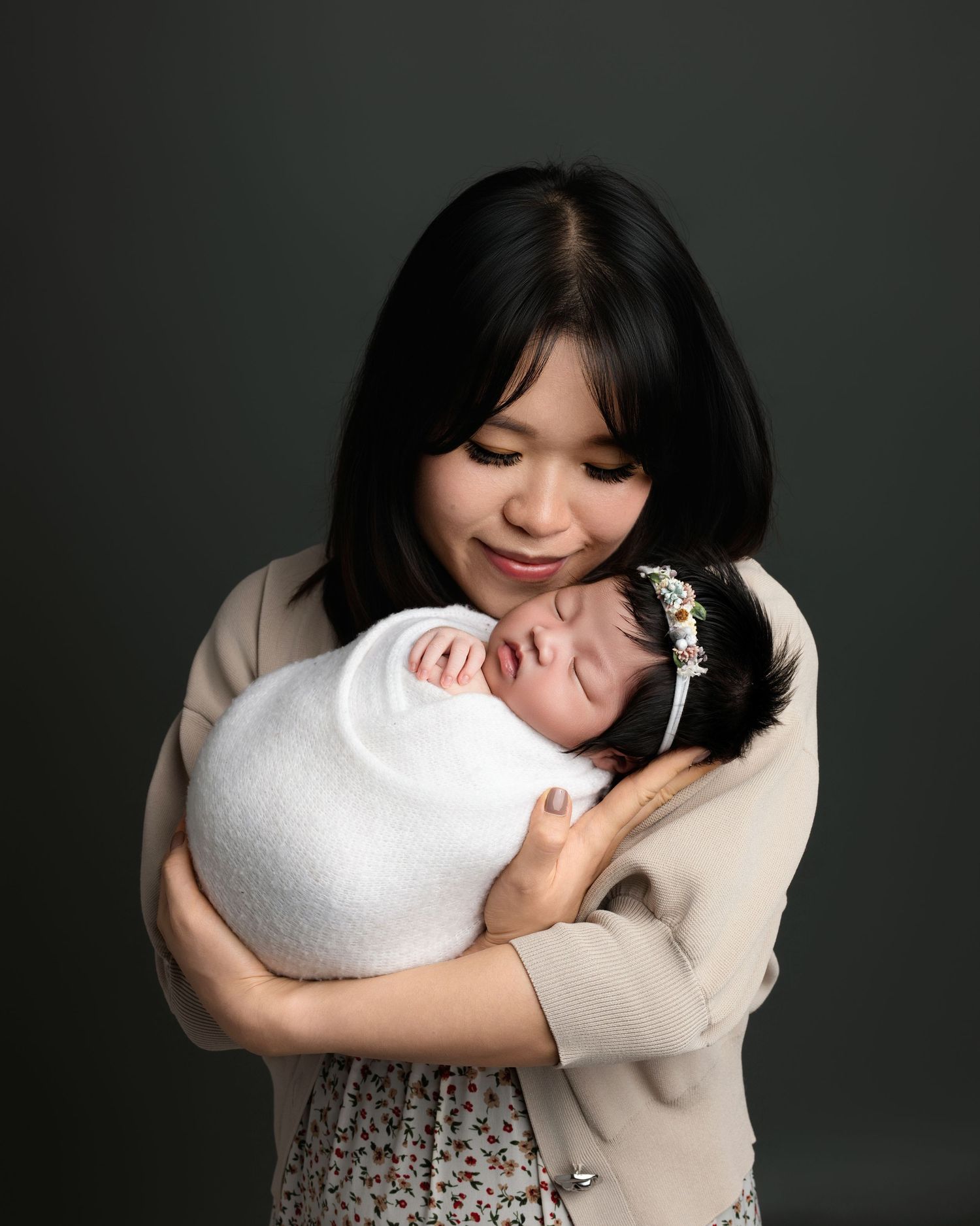 Maternity portrait series with woman in floral dress holding white pillow against dark background.