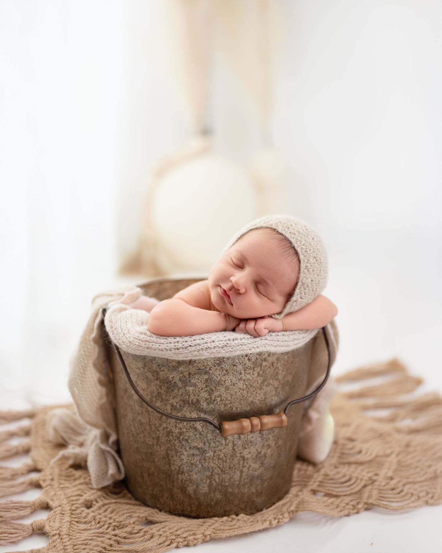 Sleeping newborn baby nestled in rustic wooden bowl on textured fabric.