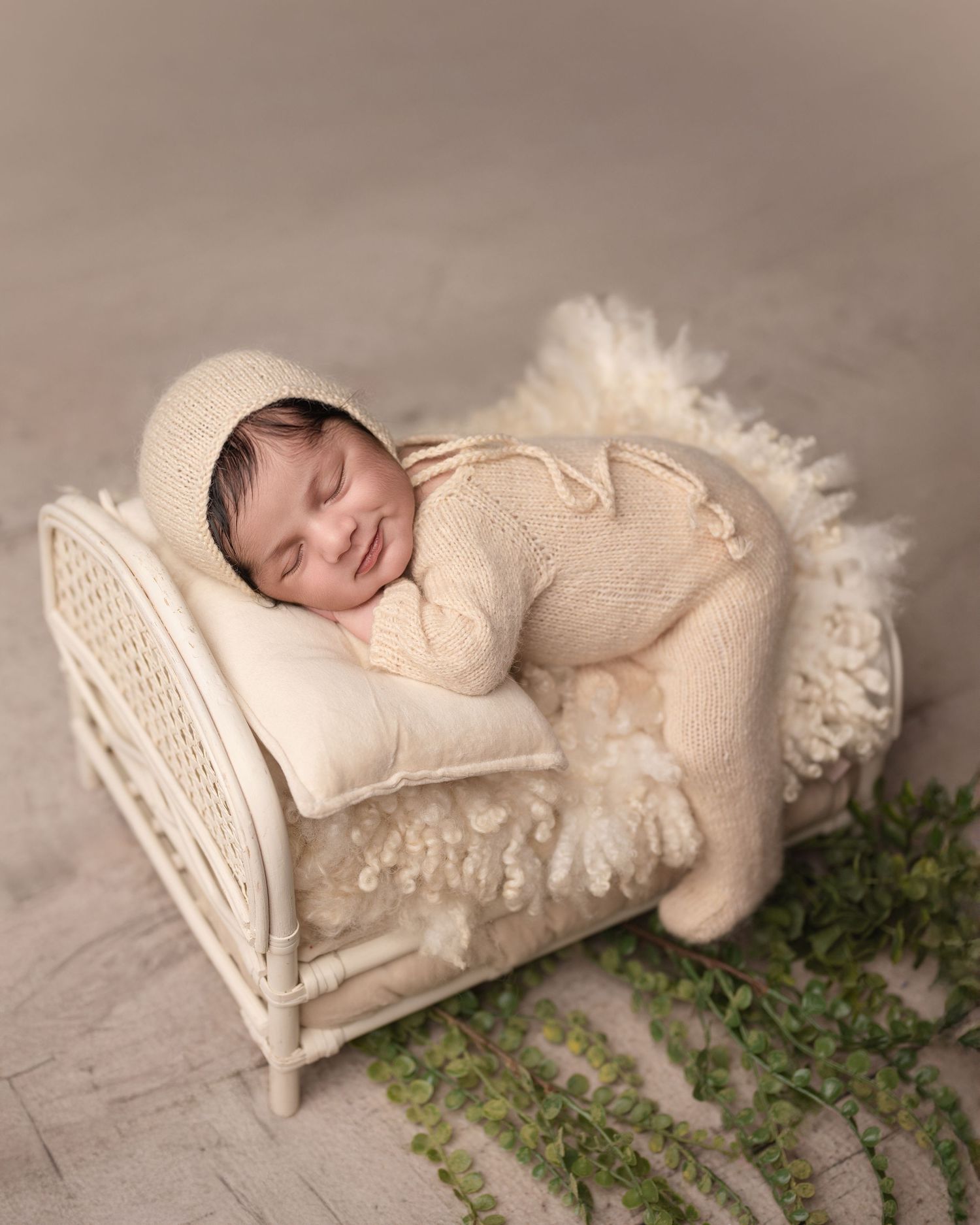 Baby sleeping on white knit blanket with delicate lace details and greenery accents.