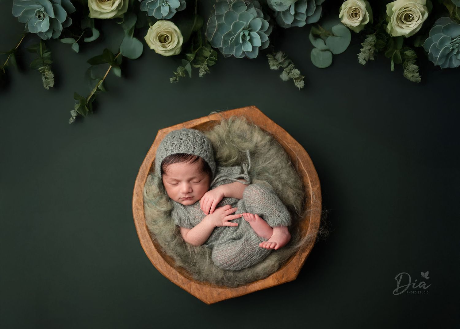Newborn portrait with baby sleeping in wooden bowl surrounded by roses and eucalyptus.