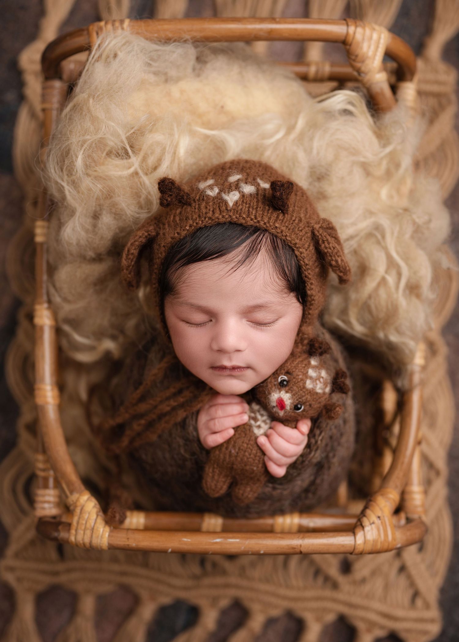 Sleeping baby in brown knit hat resting in vintage wooden basket with soft textures.