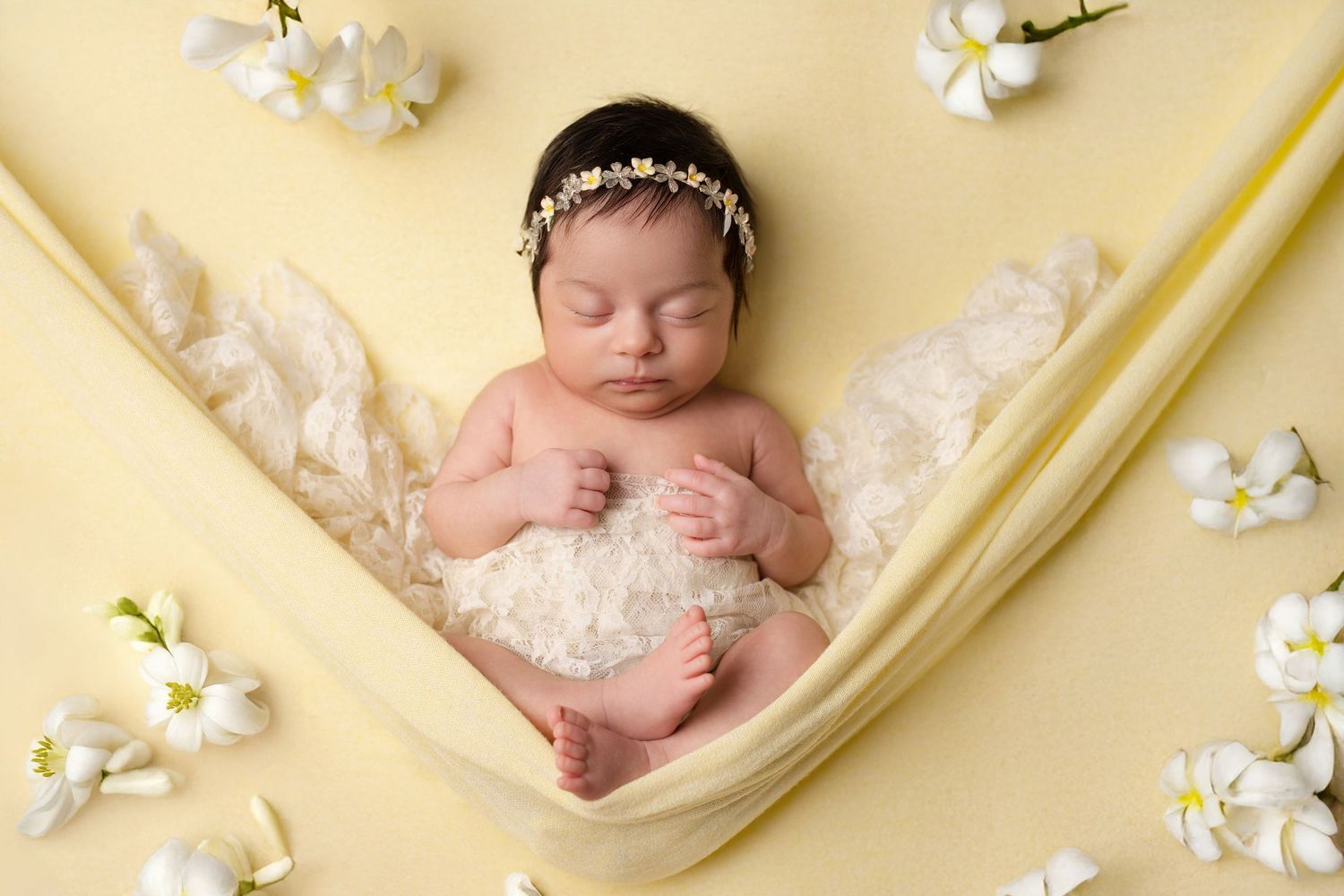 Newborn photography setup with baby sleeping on yellow backdrop surrounded by white flowers.