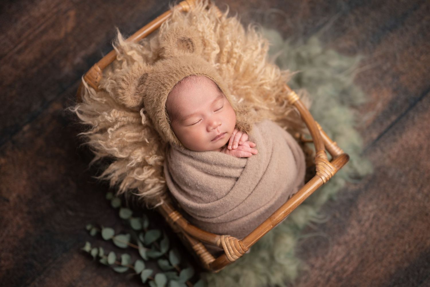 Newborn photography series featuring baby wrapped in beige fabric on rustic wooden backdrop.