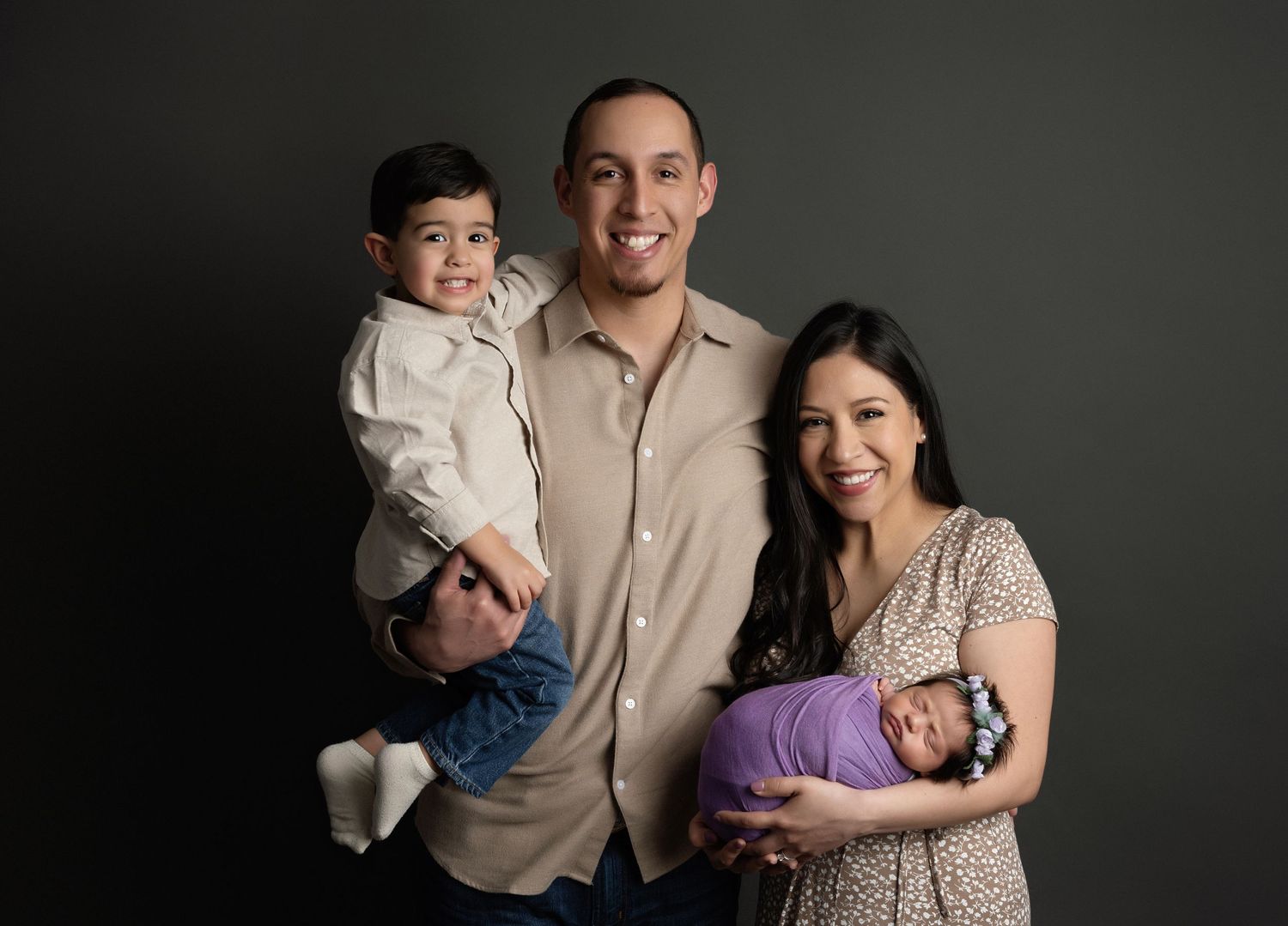 Professional family portrait session against dark background with moody lighting.