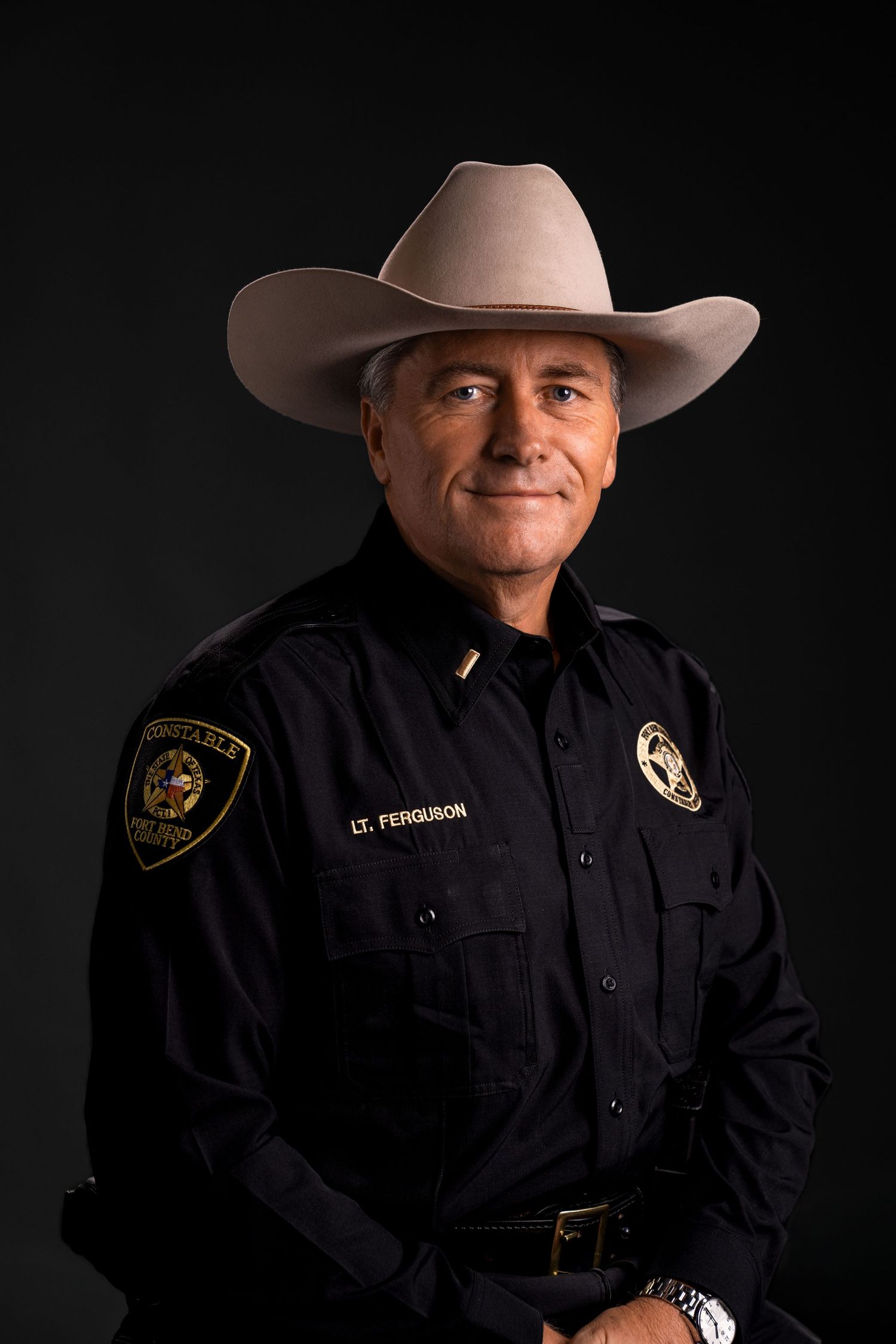 Professional portrait of law enforcement officer in uniform and cowboy hat against dark background.