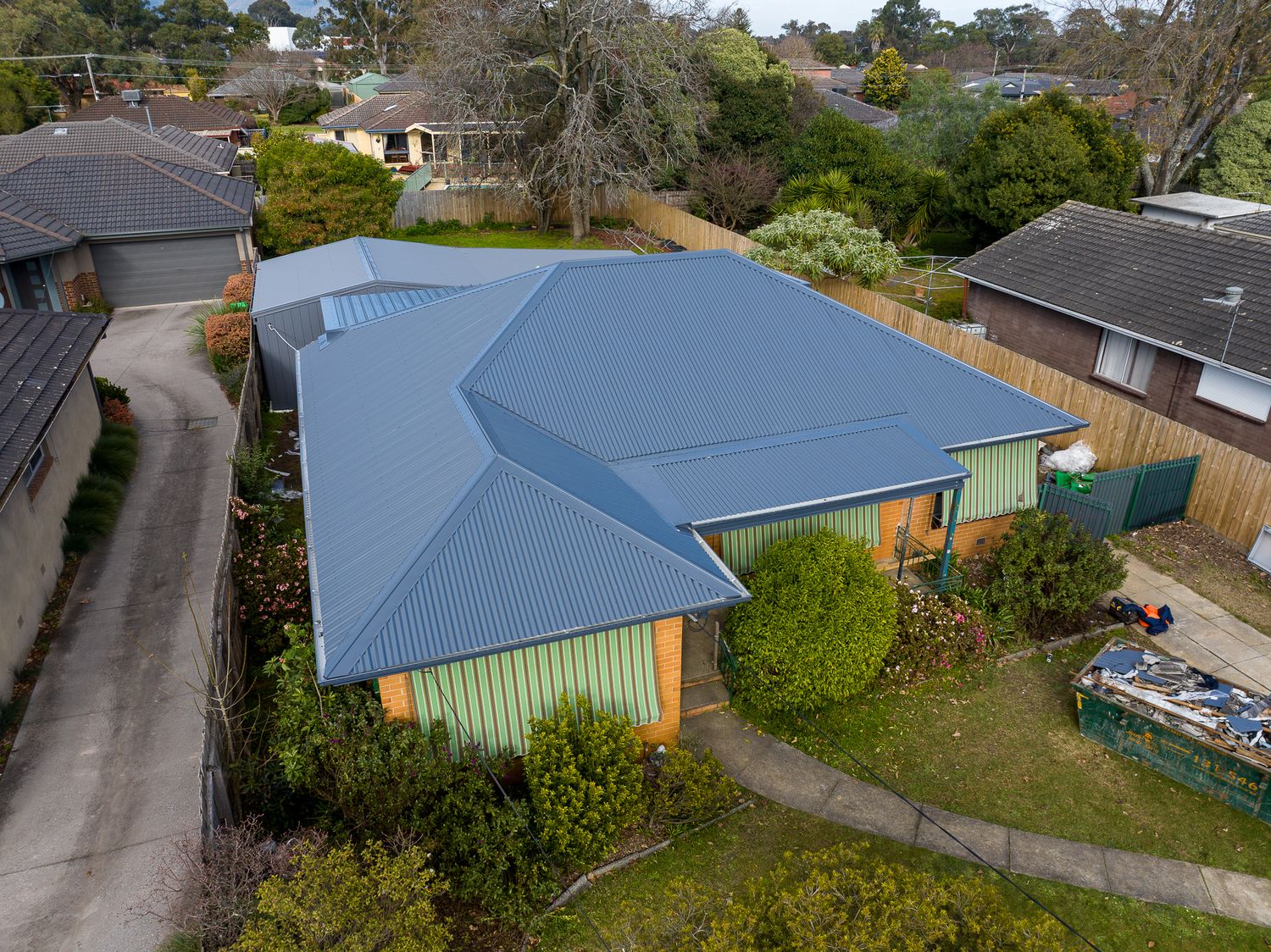 Aerial view of modern home with grey metal roof surrounded by established trees and garden in suburban setting.