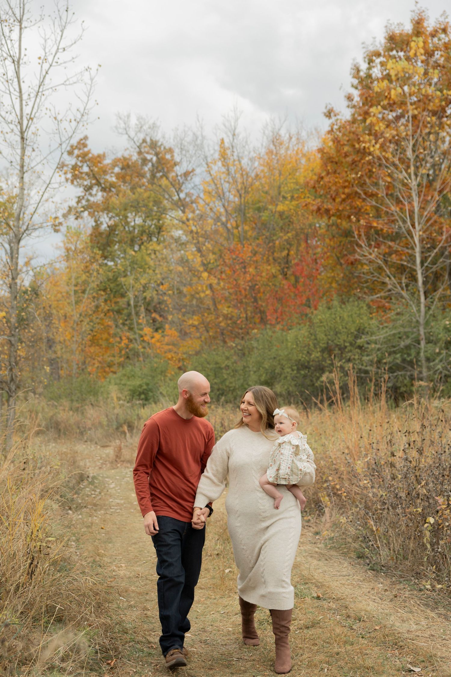 family wearing fall colors holding their 6 month old daughter in a field in Beverly Hills Birmingham michigan in fall