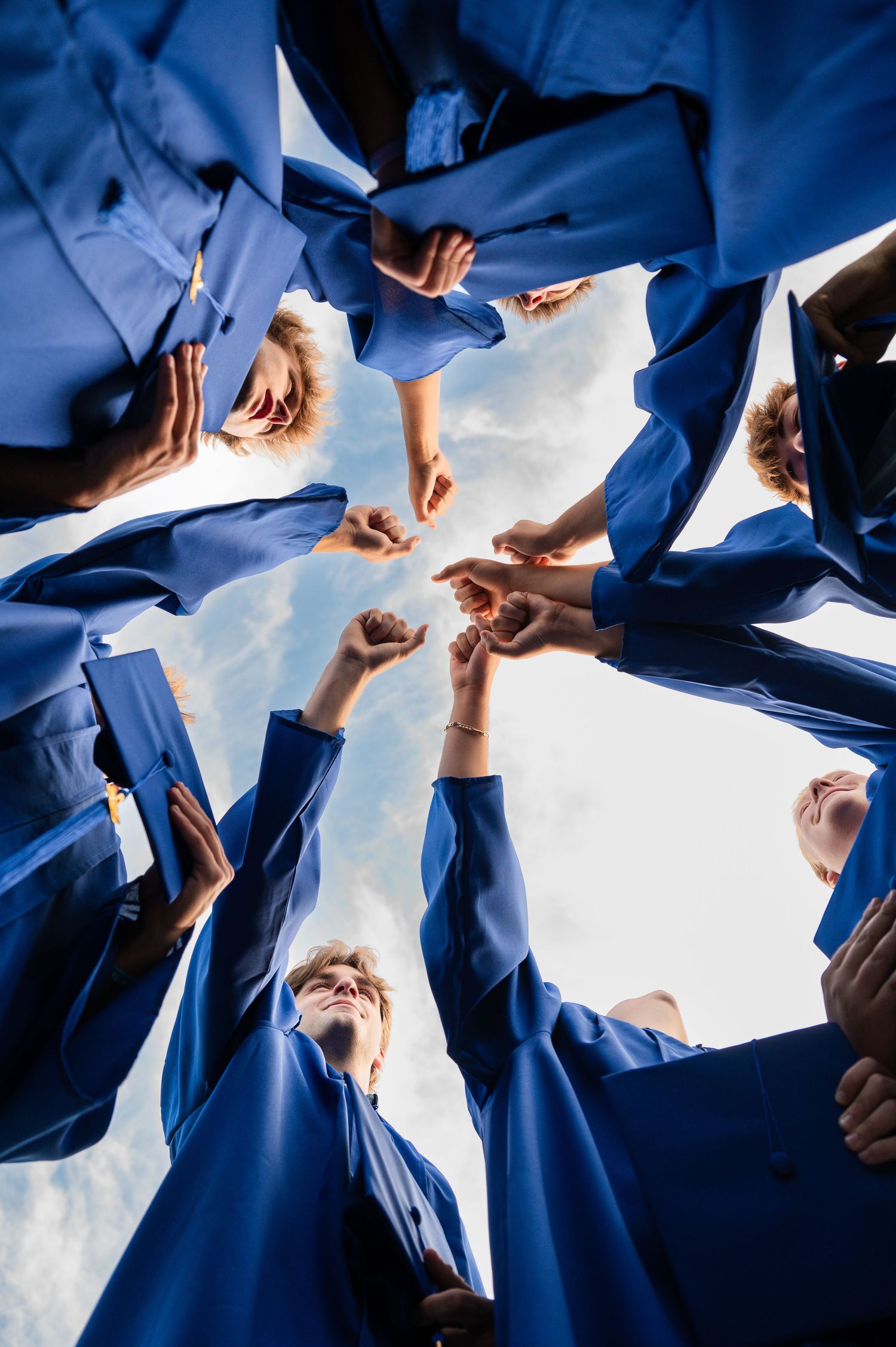 Graduates in blue gowns forming a circle viewed from below against blue sky.
