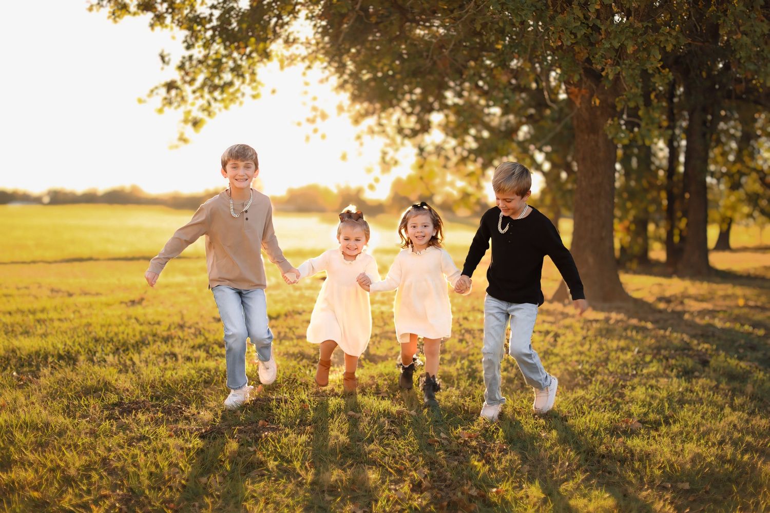 Children running and playing together in a grassy field at sunset.