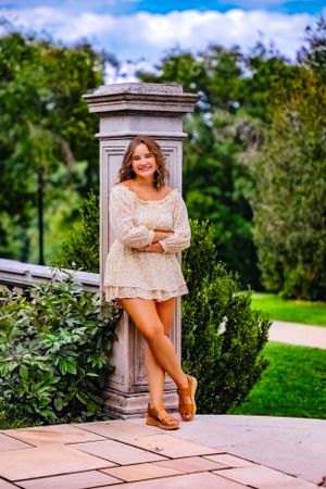 High school senior posing confidently outdoors with a natural smile, dressed in stylish attire, with soft golden sunlight highlighting their
