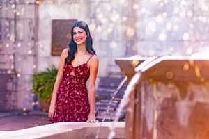senior girl leans against fountain scattered light and water surrounds her