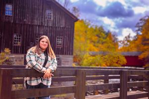 Senior portrait posed outdoors, girl lazily loses on railing with waterfall in distance background